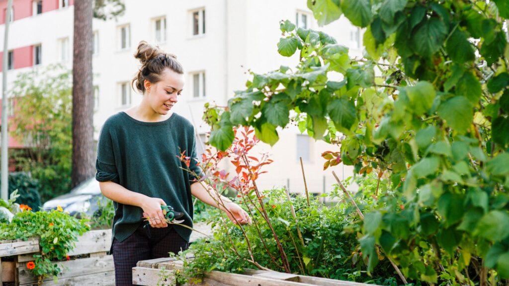 Nesting Immobilien Develeopment. Junge Frau die sich um ihre Pflanzen im Garten kümmert.